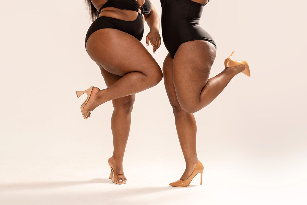 Photo of real, superb, plus size, dark skinned two womens bodies. Concept of body acceptance, body positivity. Legs in high heels.