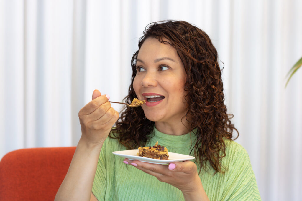 Vrouw met donkere krullen neemt een hap van de vegan blondie