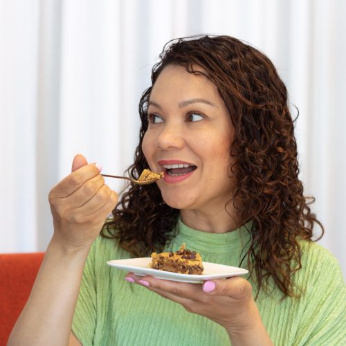 Vrouw met donkere krullen neemt een hap van de vegan blondie